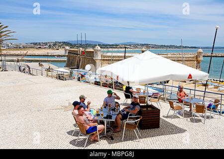 Vista in elevazione del Ponta da Bandeira Fort con i turisti in un momento di relax a un cafe' sul marciapiede in primo piano, Lagos, Algarve, Portogallo, dell'Europa. Foto Stock