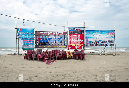 Nur, Iran - 25 Luglio 2016 : sedie impilate e pubblicità locale poster su una spiaggia deserta dal Mar Caspio Foto Stock