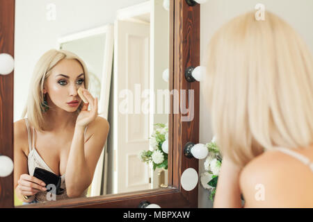 Giovane donna bionda applicare il trucco. Bella donna cerca in corrispondenza dello specchio e tenuta scatola di polvere Foto Stock