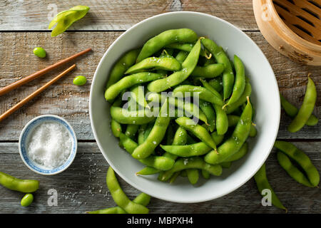 Freschi cotti al vapore edamame cosparso con sale marino su un rustico tavolo. Foto Stock