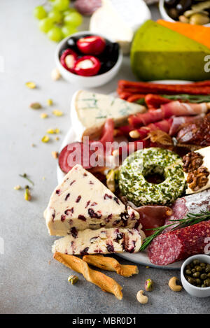 Italiano tradizionale di antipasto, tagliere con salame, freddo carne affumicata, prosciutto, prosciutto, formaggi, i capperi e le olive su sfondo grigio. Il formaggio e la carne antipasto. Foto Stock