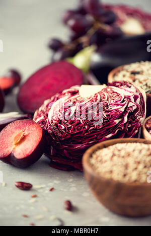 Pulire il concetto di mangiare. Materie vegetali viola sul cemento grigio Sfondo. Melanzana violetta, barbabietole, cavolfiore, viola, fagioli, prugne, cipolla, uva, quinoa, riso. Ingredienti per la cottura, spazio di copia Foto Stock