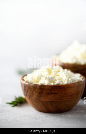 In casa cottage cheese nella ciotola di legno, rosmarino verde su sfondo grigio. Spazio di copia Foto Stock