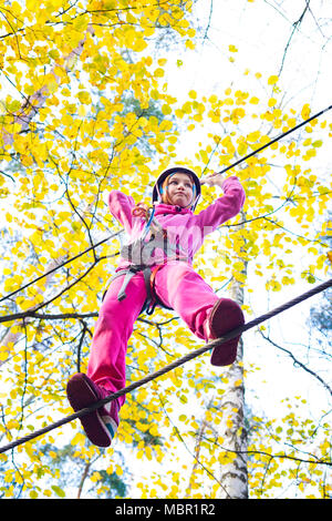 Giovane ragazza nel cablaggio di arrampicata e cercando strutture in un parco avventura. Foto Stock