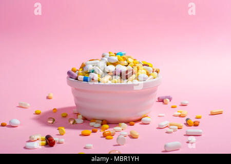 Ciotola piena di pillole colorate su sfondo rosa. Composizione creativa. Foto Stock