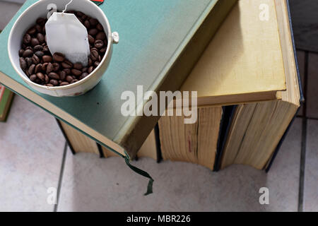 Una tazza di tè sulla pila di vecchi libri polverosi Foto Stock