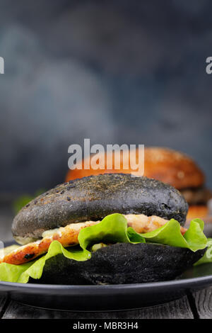 Cucinata fresca hamburger con rotolo di colore nero, verdure e salmone cotoletta. Sandwich fatti in casa closeup con spazio per il testo Foto Stock
