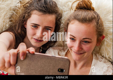 Felice di due ragazze adolescenti prendendo un selfie indoor con uno smartphone. Foto Stock