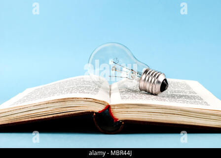 Lampadina della luce sul libro aperto isolata su uno sfondo blu Foto Stock