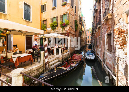 Molti visitatori in tipico piccolo cafe a Venezia vicino al canal con gondole e barche Foto Stock