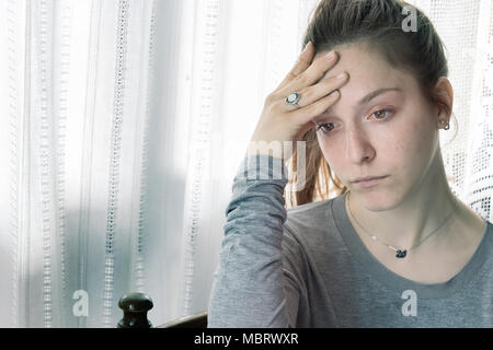 Ragazza adolescente quasi a piangere, triste a casa con la sua mano sulla fronte guardando verso il basso. Foto Stock