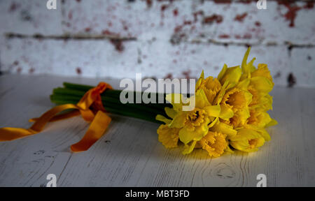 Un mazzetto di narcisi legate con un nastro arancione posto su un bianco pavimento in laminato. Foto Stock