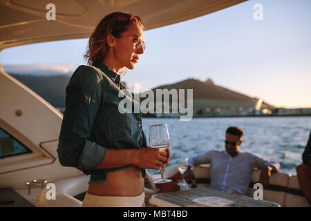 Bella donna con su yacht con la bevanda. Donna festa sulla barca privata con amici in background. Foto Stock