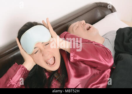 Ritratto di donna irritata bloccando le orecchie con le mani mentre l'uomo è il russamento sul letto. In ambienti interni Foto Stock