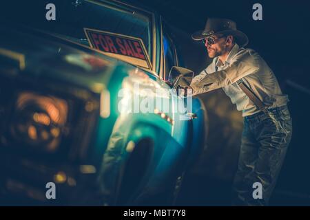 Western Cowboy di usura nel suo 30s cercando una nuova vettura. Guardare all'interno di American Classic Car. In vendita segno sul parabrezza. Foto Stock