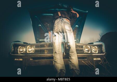 Il fissaggio rotto auto classica sul lato della strada di campagna da uomini caucasici che indossa lo stile occidentale e vestiti. Il cowboy e la sua corsa Vintage. Foto Stock