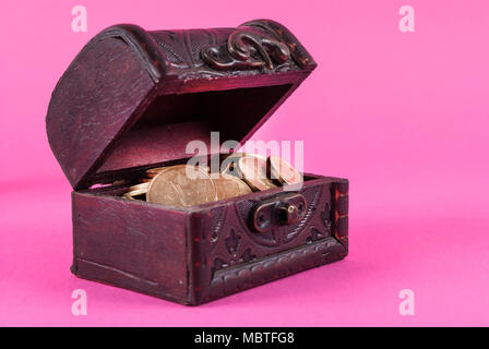 Monete in una vecchia scatola di legno su un sfondo rosa Foto Stock