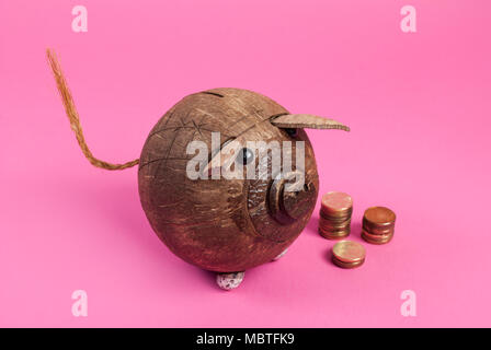 Carino salvadanaio realizzato da noce di cocco e coin isolato su sfondo rosa Foto Stock