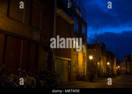 Debolmente illuminata strada laterale con una drammatica blu cielo con una frattura. Alcune luci di strada illuminare i vecchi edifici e le biciclette che linea il vicolo. Foto Stock