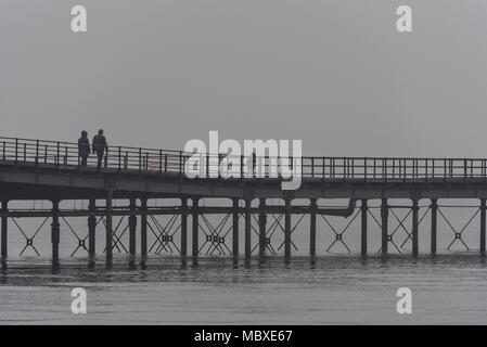 La nebbia e la foschia sopra Essex non scoraggiare gli escursionisti a passeggiare sul molo di Southend nel torbido estuario del Tamigi o giocando sulla spiaggia Foto Stock