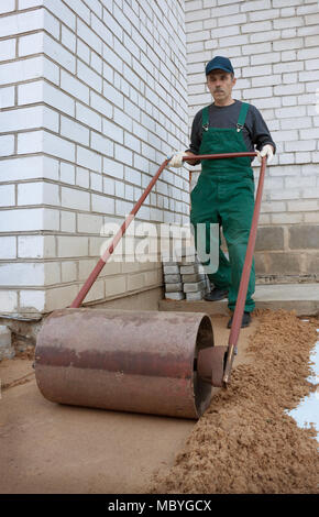La compattazione del suolo rullo manualmente prima di creare il marciapiede Foto Stock