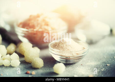 Mix di diversi tipi di sale sul cemento grigio Sfondo. Sali marini, nero e rosa himalayana di cristalli di sale, polvere, rosmarino. Sale le sfere di cristallo del Mar Morto. Copia dello spazio. Tonico effetto luce solare Foto Stock