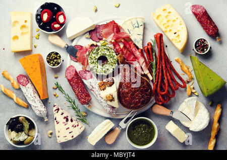 Tagliere con il freddo carne affumicata, prosciutto, salame, assortimento di formaggi, grissini, capperi, olive su pietra grigia sullo sfondo. Il formaggio e la carne antipasto. Vista superiore, copia dello spazio, laici piatta Foto Stock