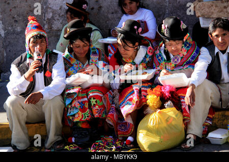 Tradizionalmente condita adolescenti peruviane sono seduti sul lato della strada e di mangiare e di bere e godere di un festival di folklore in Arequipa, Perù Foto Stock