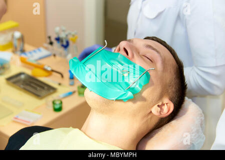 Il giovane uomo nel riunito dentale guarisce il dente con l'uso di un sistema di dighe in gomma con lattice sciarpe e graffe metalliche, la produzione di photop Foto Stock