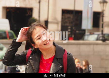 Una giovane donna in posa per avere la sua fotografia scattata in Trafalgar Square a Londra con un grande sorriso sul suo viso Foto Stock