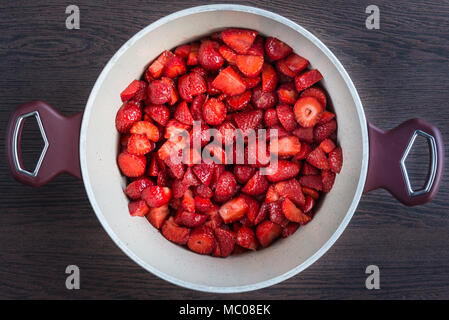 Vista dall'alto di una pentola con fragole fresche tagliate a pezzi, preparato per una confettura di fragole di cottura. Foto Stock