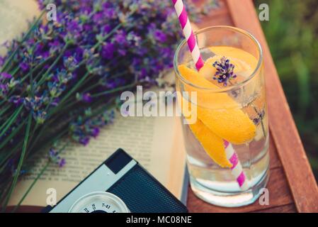 Un bicchiere di limonata fresca, cameta vintage, un libro e appena tagliato Lavanda fiori su una sedia in legno. Foto Stock