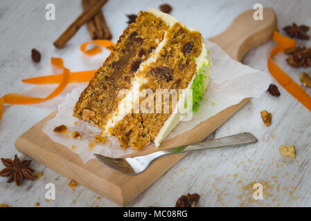 In prossimità di una casalinga torta di carote con uvetta, noci e cannella sopra bianco sullo sfondo di legno. La glassa di formaggio cremoso. Foto Stock