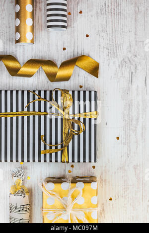 Confezioni regalo avvolto in bianco e nero a strisce e golden punteggiato di carta e materiali di imballaggio su di un legno bianco sfondo vecchio. Foto Stock