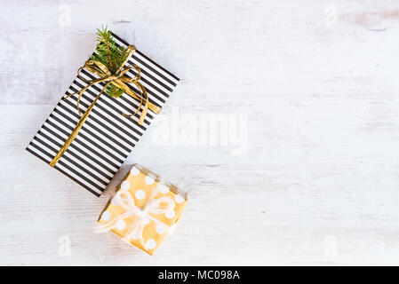 Confezioni regalo avvolto in bianco e nero a strisce e golden tratteggiata su carta bianca di sfondo di legno. I regali di Natale. Spazio vuoto. Foto Stock