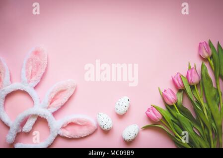 Vista dall'alto di uova di Pasqua, rosa tulipani e due bianchi e soffici orecchie di coniglietto su sfondo rosa. Concetto di pasqua sfondo.Copia dello spazio. Foto Stock