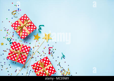 Vista dall'alto di una rossa tratteggiata scatole regalo, golden bacchette magiche e colorati di coriandoli e nastri su sfondo blu. Celebrazione del concetto. Copia dello spazio. Foto Stock