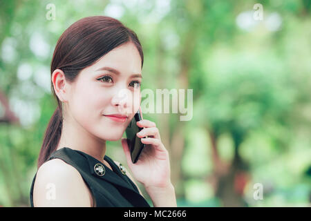 Bella smart business look donna asiatica chiamando con smart phone nel parco Foto Stock
