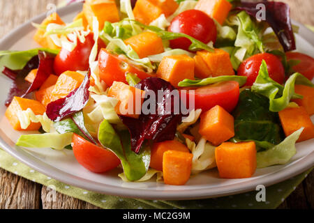 In casa insalata di patate dolci con pomodori, lattuga, cipolla e erbe aromatiche close-up su una piastra su un piano orizzontale. Foto Stock