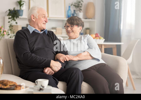 Felice nonni seduti insieme su un lettino, parlando e avvolgente Foto Stock