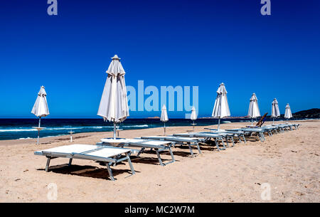 Righe di colore bianco e grigio chiuso ombrelloni e sedie a sdraio sulla spiaggia sarda Foto Stock