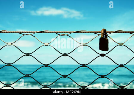 Vecchio arrugginito bloccano sulla recinzione in ferro con il blu del mare sullo sfondo Foto Stock