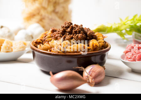 Primo piano orizzontale dei tradizionali piatti di pasta italiana con il ragù alla bolognese con tutti gli ingredienti accanto ad essa, la pasta è servita in una terracotta piastra marrone su un Foto Stock