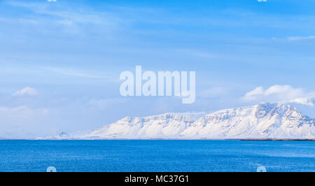 Islandese il paesaggio costiero, montagne innevate sull orizzonte sotto il cielo blu. Reykjavik, Islanda Foto Stock