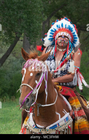 In guerriero Comanche abbigliamento equitazione cavallo di castagno decorate con pitture di guerra attraverso la foresta Foto Stock