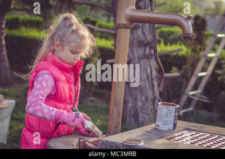 Adorabile ragazza bionda verniciatura a pennello di un pozzo nel giardino Foto Stock