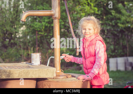 Adorabile ragazza bionda verniciatura a pennello di un pozzo nel giardino Foto Stock