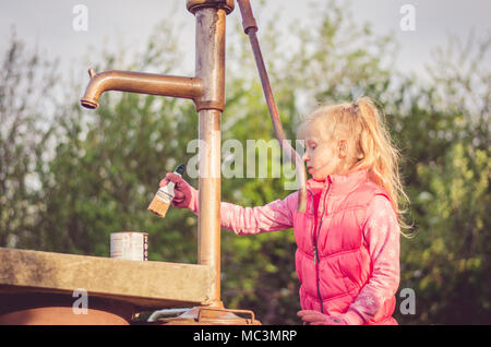 Adorabile ragazza bionda verniciatura a pennello di un pozzo nel giardino Foto Stock