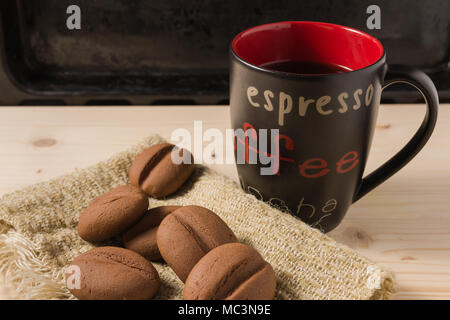 Un caffè in una tazza nera con i chicchi di caffè forma di cookie Foto Stock