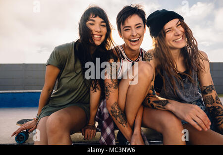 Ritratto di tre skater femmina avente un grande tempo all'aperto. Il gruppo di donne sedute a skate park e ridere. Foto Stock